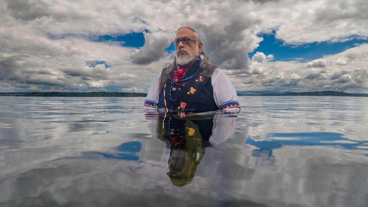 Photo of Timothy White Eagle waist deep in water amidst a field of clouds
